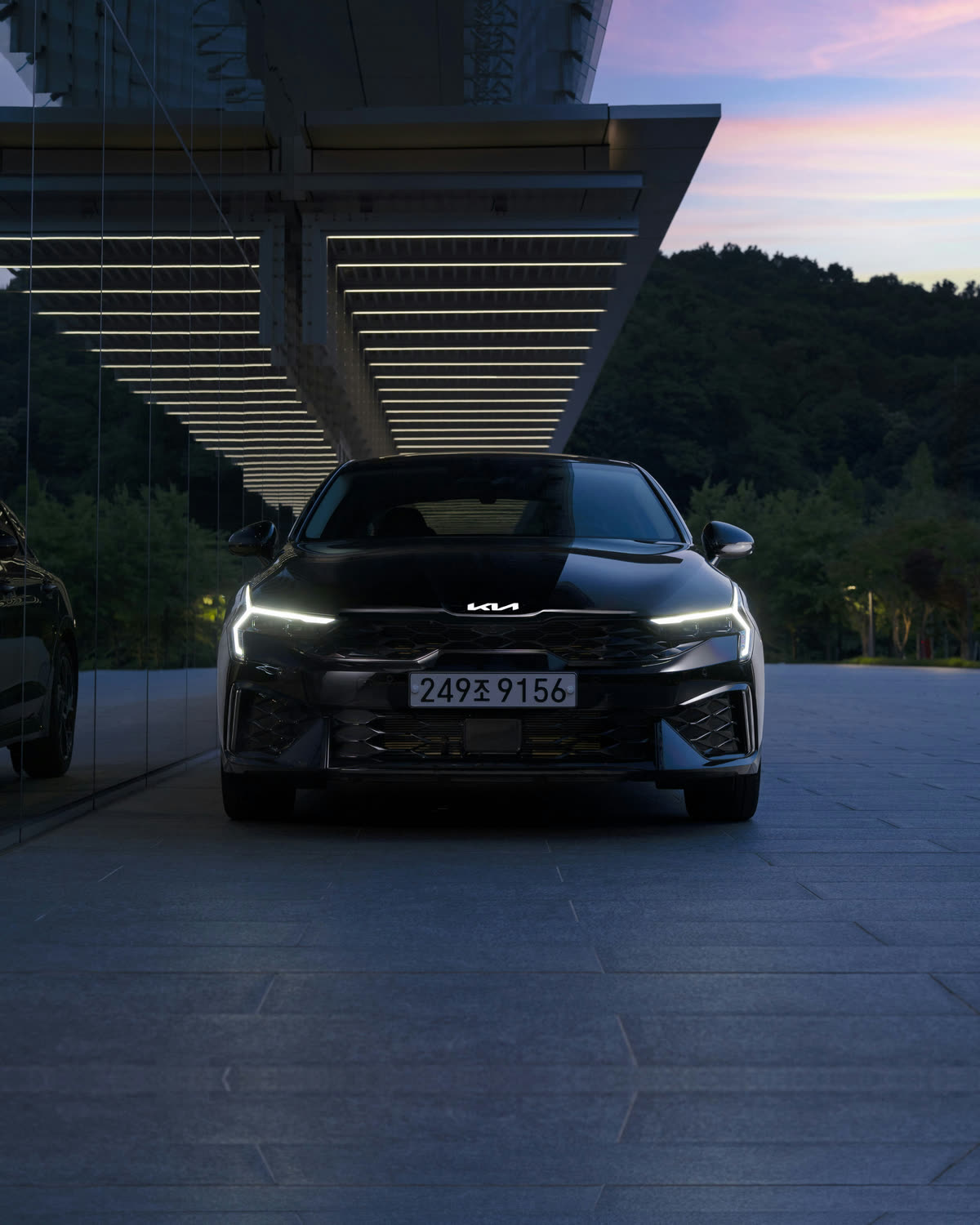 Kia K5 у современного здания на закате